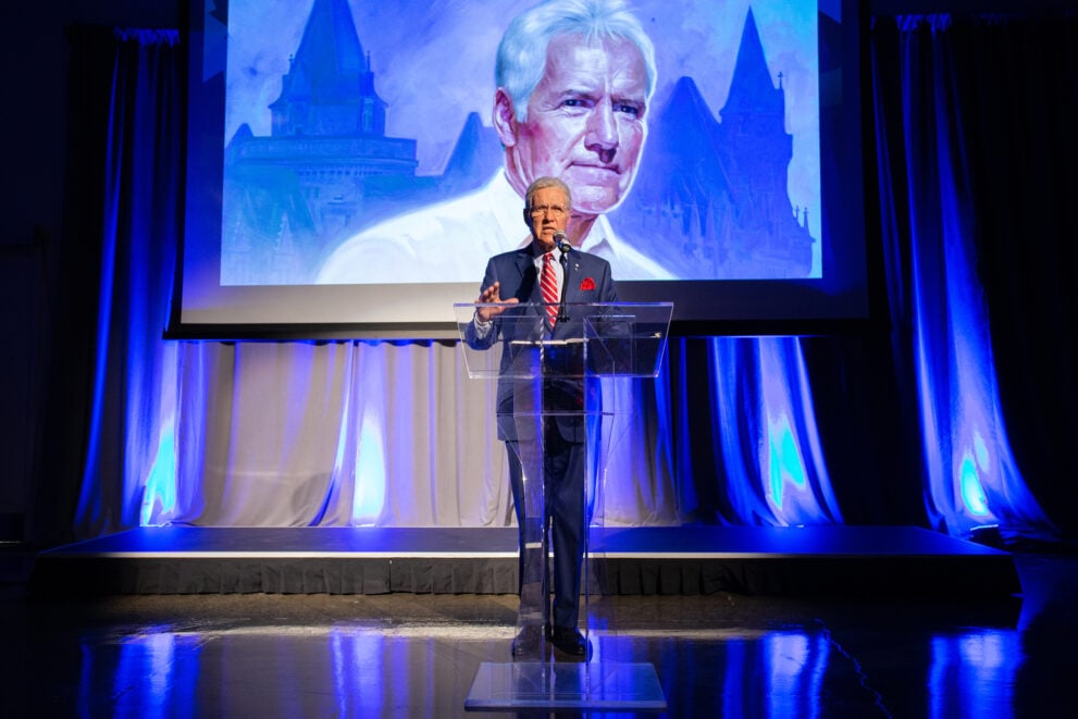 Alex Trebek stands at a podium