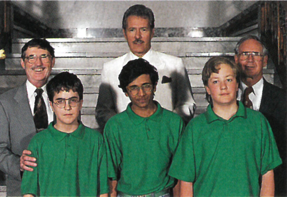 An old photo of Alex Trebek and two adult men posing with three young boys in green polo shirts