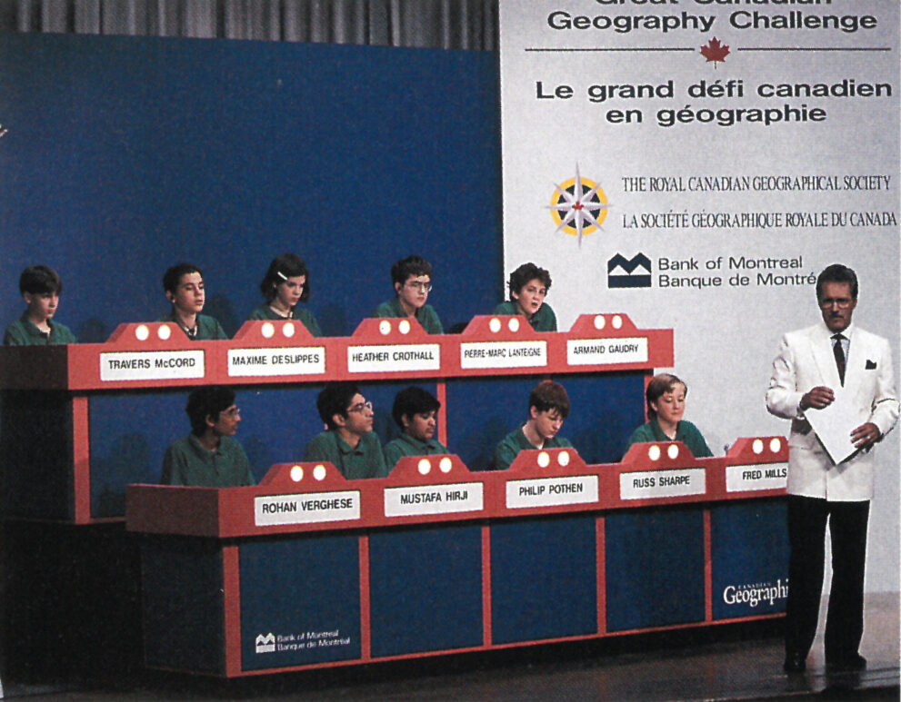 Alex Trebek stands in front of the stands of the geography competition