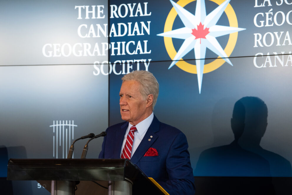 Alex Trebek speaks at a podium with the RCGS logo displayed behind him