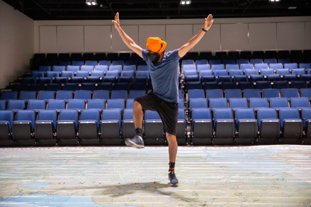 Gurdeep Pandher, who wears an orange turban, blue shirt and shorts, dances on a Giant Floor Map of Ontario in the Society's auditorium